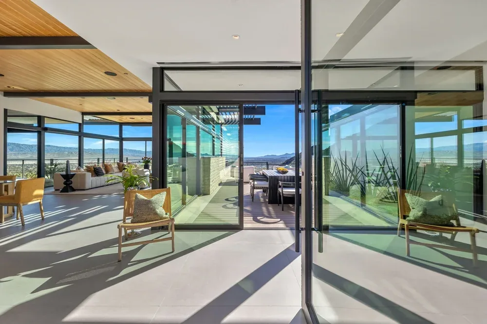 Sliding walls of glass opening a living room onto a terrace and the valley beyond.