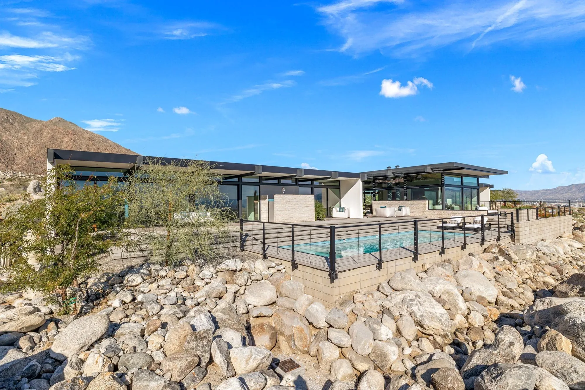 A glass-walled house and lap pool set on a boulder shelf beneath the ridge.